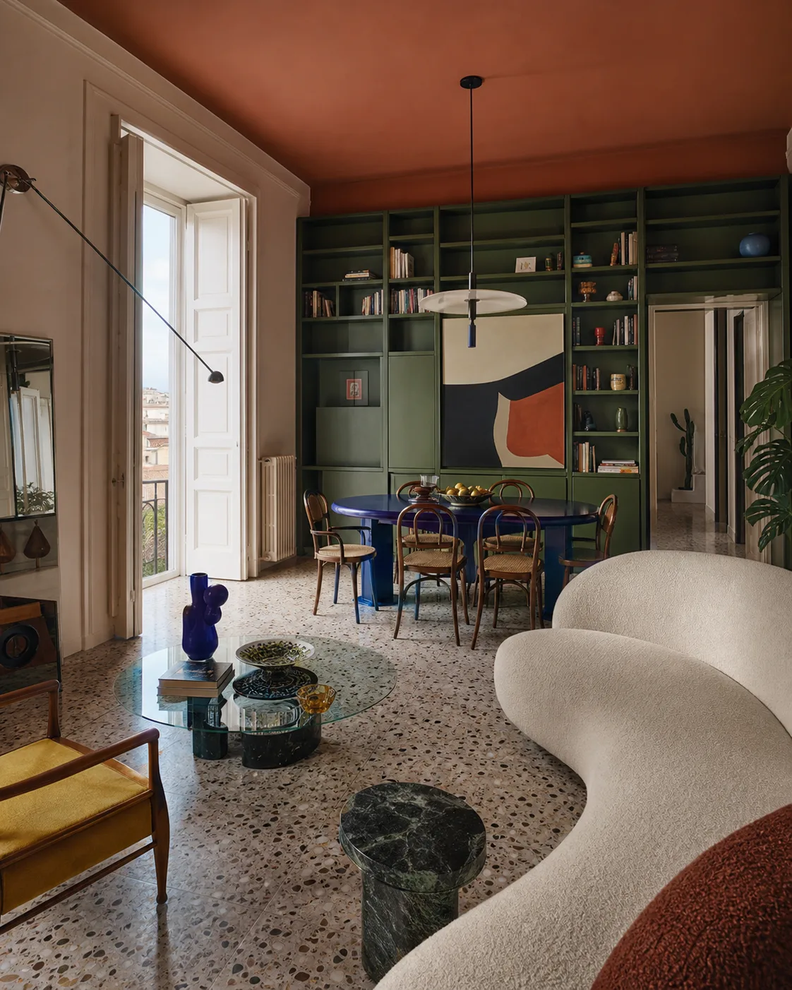 Soggiorno personale con libreria verde, soffitto terracotta e tavolo blu